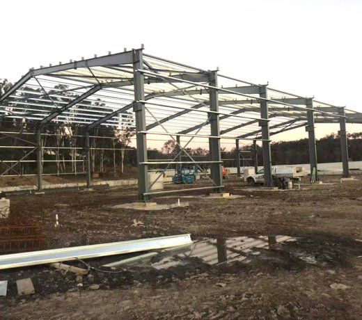 Projet de structure métallique australienne de 80 m x 25 m x 12 m sous un ciel dégagé : érection des fondations des colonnes d’acier et formation de la charpente du bâtiment industriel
