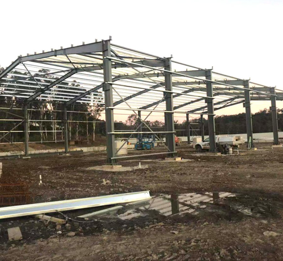 Projet de structure métallique australienne de 80 m x 25 m x 12 m sous un ciel dégagé : érection des fondations des colonnes d’acier et formation de la charpente du bâtiment industriel