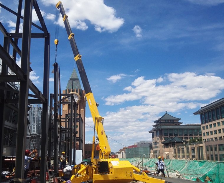 Spider crane performing steel erection hoisting on a building rooftop in a commercial district.