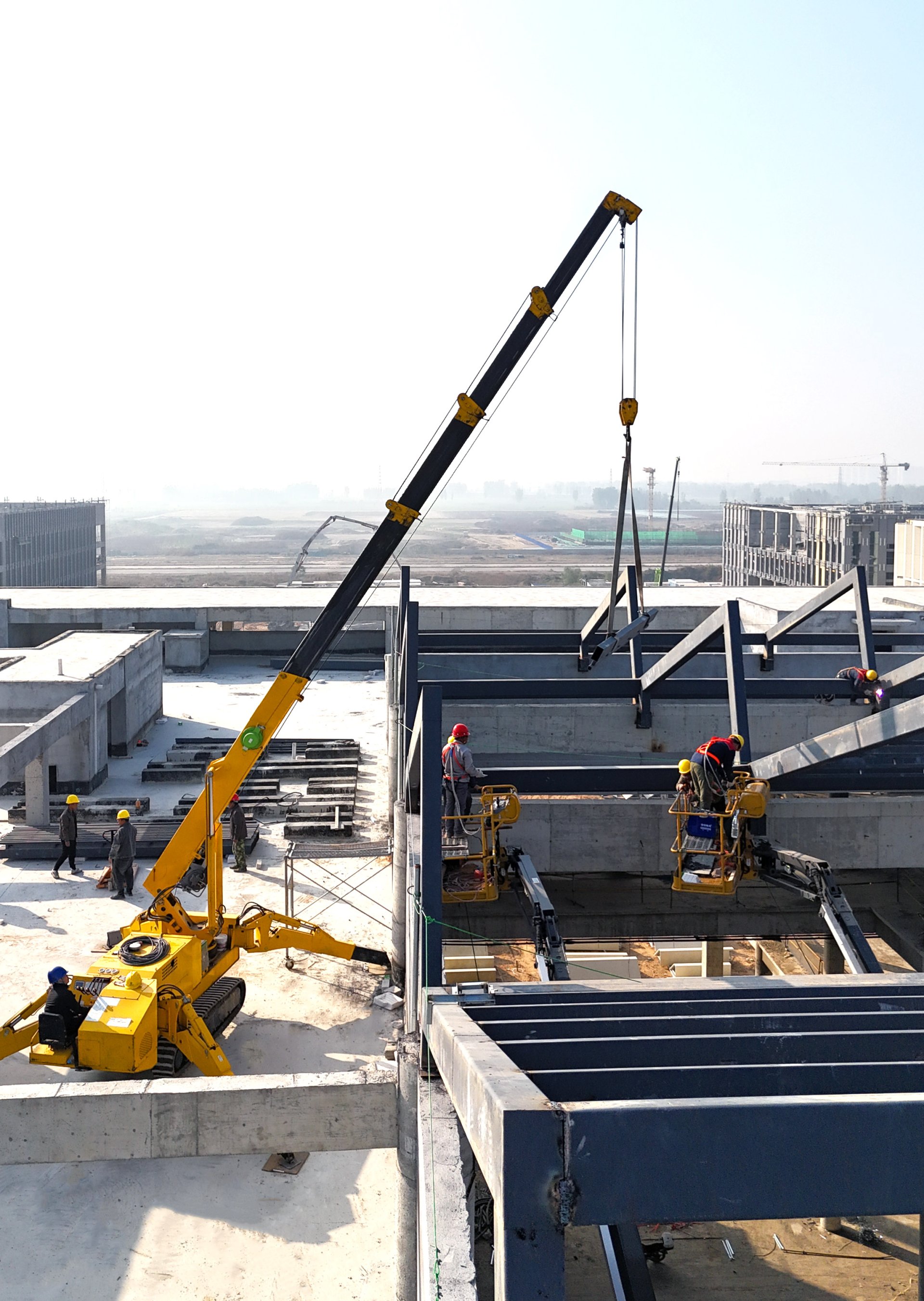 Compact crawler crane lifting heavy beams during steel structure installation on a commercial job site.